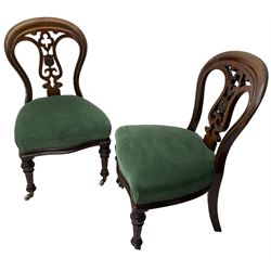 Pair of Victorian mahogany dining chairs, moulded balloon back with scrolled and pierced splat with central shield, upholstered in green fabric, on turned and fluted front supports with brass cups and castors 