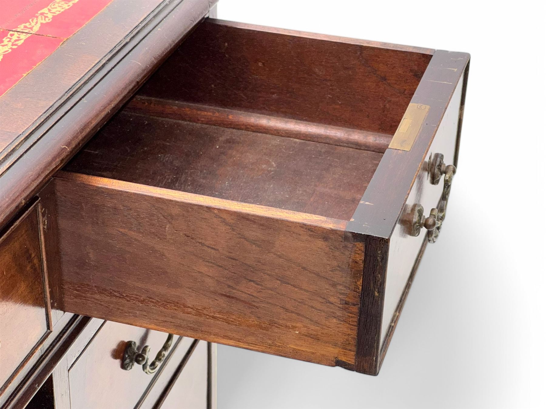 Georgian design mahogany kneehole desk, moulded rectangular top with red gilt-tooled leather writing surface, over an arrangement of nine cock-beaded drawers with brass swan neck handles, on bracket feet