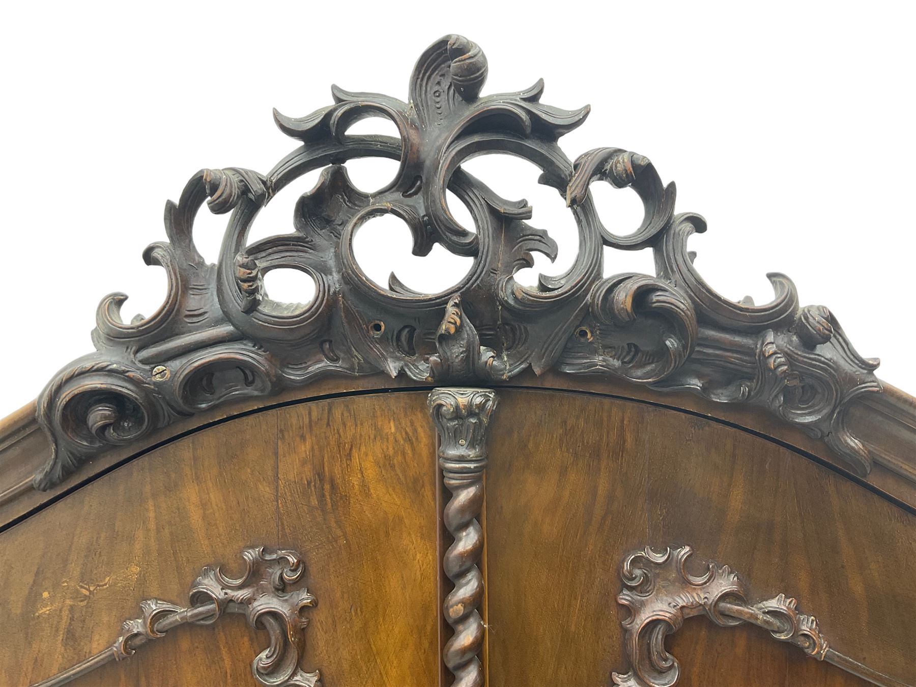Early 20th century Italian walnut armoire wardrobe, the pierced and scrolling pediment carved with acanthus leaf detail, flanked by two scrolling cartouche with matching corbels below, the two panelled doors with applied carved rinceaux slips, with a central spiral turned upright, enclosing single shelf and hanging rail, raised on scroll feet