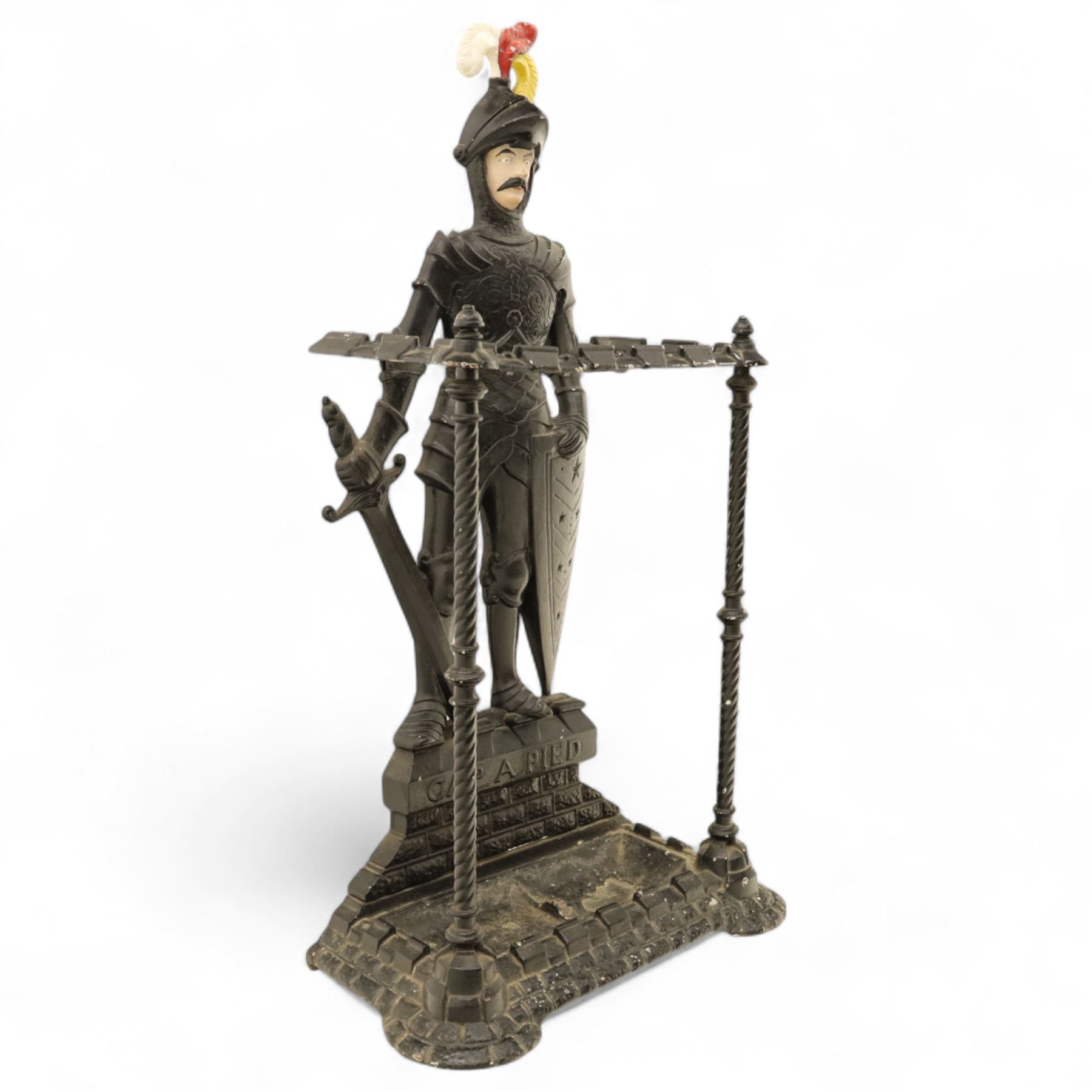 Early 20th century painted cast iron hall stand, formed as a standing armoured figure with red and yellow feathered crest, twin rails and integral drip tray with castellated edge