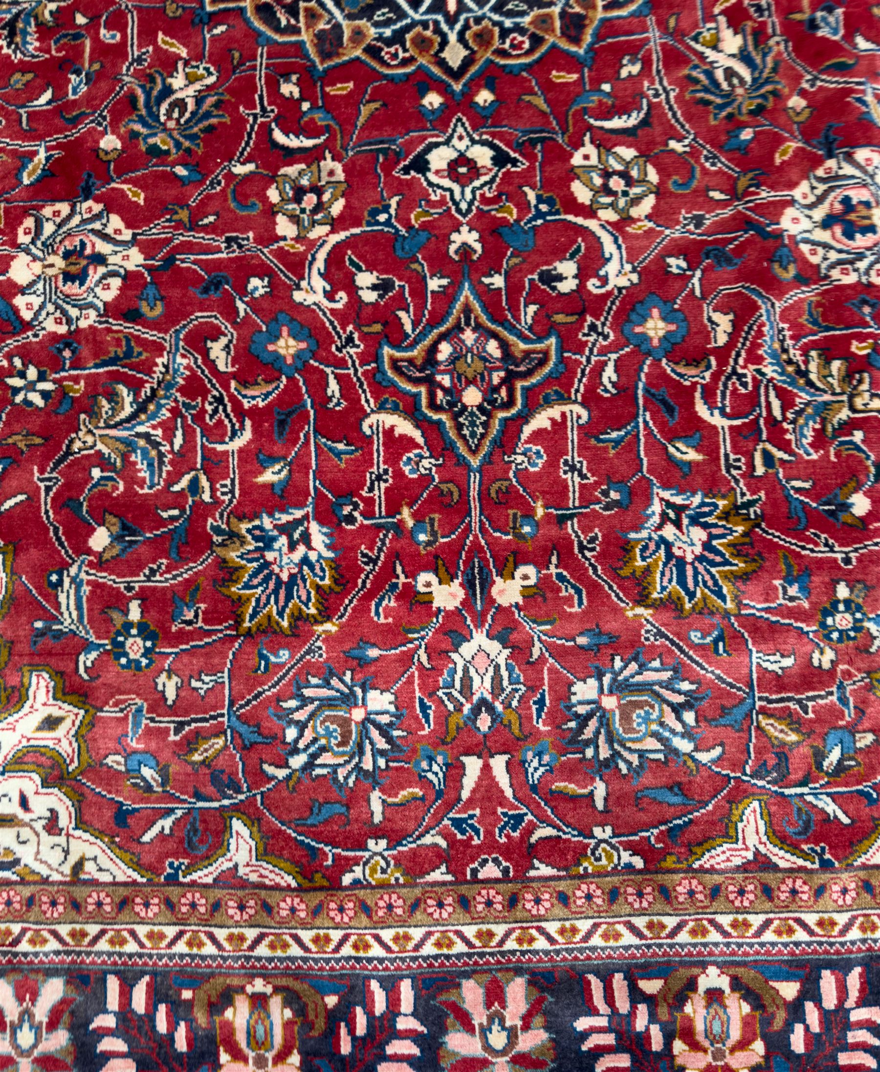 Northwestern Persian Lillihan hand-knotted carpet, madder red field with scrolling vines, rosettes, and palmettes around a central circular medallion in navy, ivory and ochre, and ivory ground spandrels within a navy border of stylized flowerheads and vines between multiple guard stripes 