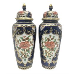 Pair of early 20th century Aynsley lidded vases, each painted with floral sprays, within deep blue and ornate gilt pattern borders, the conforming covers each with gilt finials, pattern no D141, both with printed marks beneath