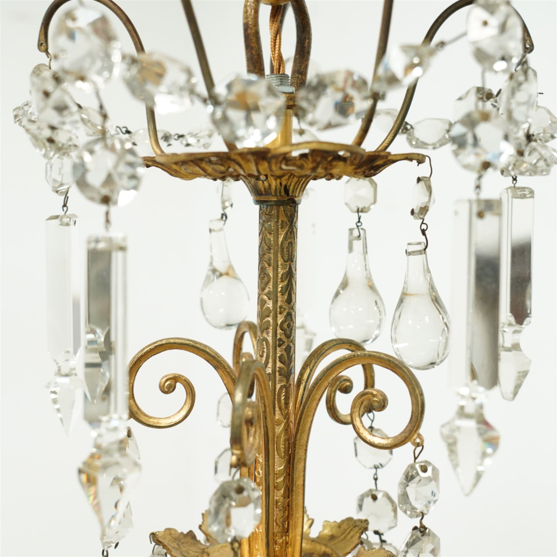 Late Victorian gilt bronze mounted crystal chandelier, ceiling rose above shaped top of trailing swags, glass crystal droplets, beneath rising curled branches and glass beads tapering down to five candle sconces, inside circular bezel fitted with drops and glass twist fluted stem, supported with an internal metal shaft above a rococo style stem holding double branches, and similar styled branches, with twelve branches fitted with candle holders and drip trays with crystal drops and cut crystal spears, the underside festooned with crystal glass swags and a bulbous fluted glass terminal and shaped finial with crystal glass swags attached to the branches, the base with pear shaped droplet graduating to the centre, wired for electricity 