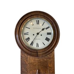 A late 19th century English oak cased wall clock retailed by R, Wilson, Nuneaton (Warx) c 1880, in figured oak case with a short spire topped door and 18” turned wooden bezel, with a 12” painted dial, Roman numerals, minute track and steel spade hands, flat bevelled glass within a brass bezel, dial pinned via a false plate to a weight driven 8- day rack striking movement striking the hours on a bell (strike components removed but present), With pendulum, weights and key.


