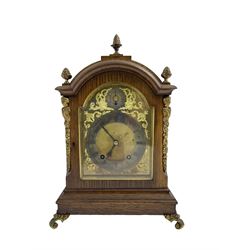 Winterhalder & Hoffmeier - early 20th century German 8-day oak cased mantle clock, case with a break arch top and brass pineapple finials, brass caryatids and sound frets to the sides, raised on scroll feet, break arch brass dial, matted centre and silvered chapter ring, with spandrels and pendulum regulation dial, twin train rack striking movement sounding the quarters on two gongs and hours on one. No pendulum or key. 