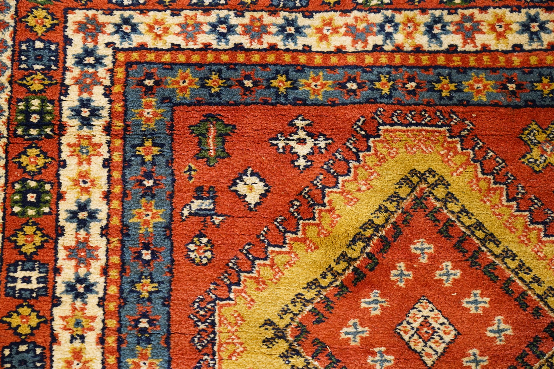 Caucasian Kazak vermillion ground rug, the sectioned field decorated with three geometric lozenge medallions surrounded by stylised plant and animal motifs, the multiple guard bands with repeating geometric design