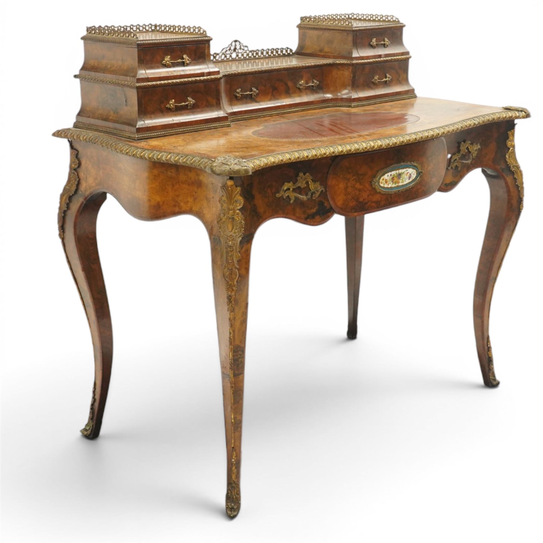 Victorian figured walnut and kingwood-banded ladies writing table, the raised superstructure with three-quarter pierced brass raised gallery back, fitted with five assorted drawers, the serpentine shaped top with oval inset leather surface, the bronze edge of egg and dart form with cartouche corners, fitted with central frieze drawer with inset Sevres-style floral ceramic plaque, raised on cabriole supports with gilt metal mounts