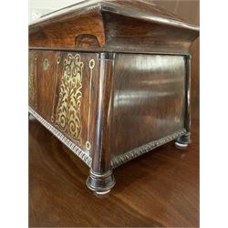 Early 19th century rosewood and brass inlaid tea caddy, of sarcophagus form, the front and hinged opening cover inlaid with brass scrolling panels, opening to reveal a compartmented interior with twin removable boxes with conforming inlaid brass detail to the hinged covers and zinc lining to the interiors, flanking a later glass mixing bowl, the whole upon four turned cylindrical feet, H21cm W36cm D20cm