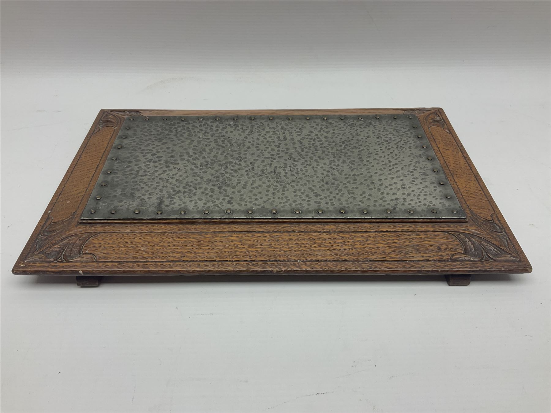 Arts and Crafts oak stand by Arthur Simpson of Kendal, of rectangular form with central hammered pewter panel, surrounded by a border with carved foliate corners, upon two bar supports, bearing label detailed 