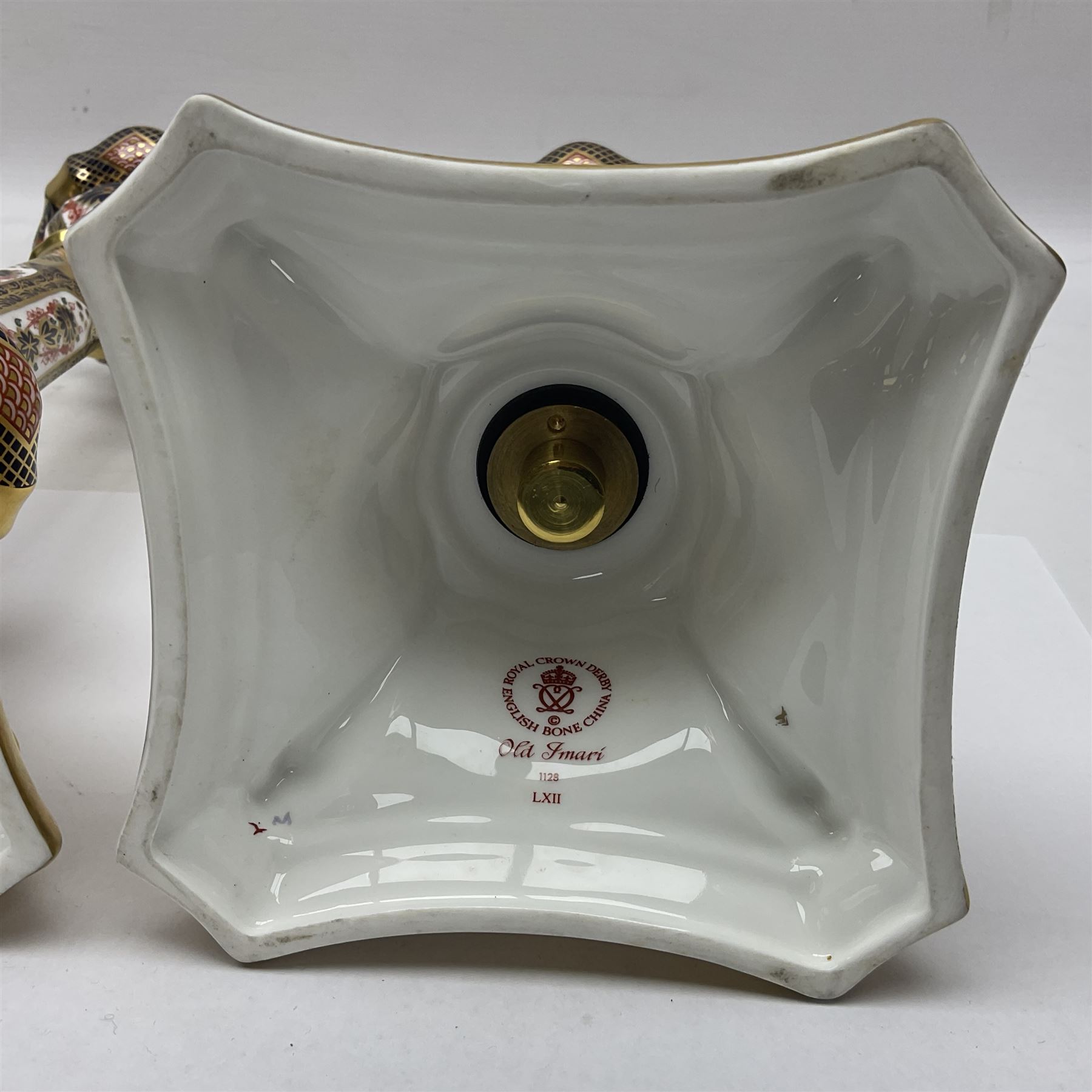 Pair of modern Royal Crown Derby Old Imari 1128 pattern candlesticks, each with shaped drip tray affixed to squat socket, upon spreading stem and canted square base with gilt dolphin edges, with printed marks beneath including Roman numeral year cypher for 2003, H26.5cm, with original boxes