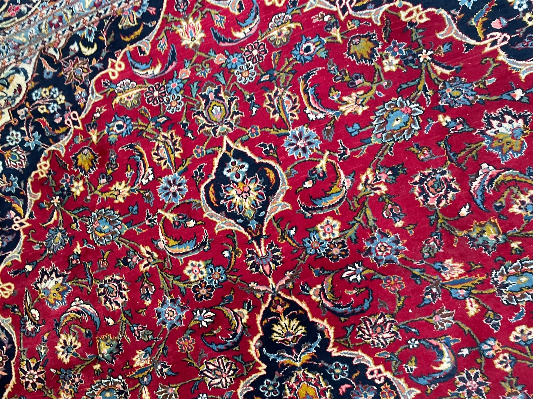 Persian Kashan crimson ground carpet, the central pole medallion decorated with flower heads, surrounded by trailing leafy branches and palmettes, scrolling border decorated with further palmettes, within floral pattern guard stripes 