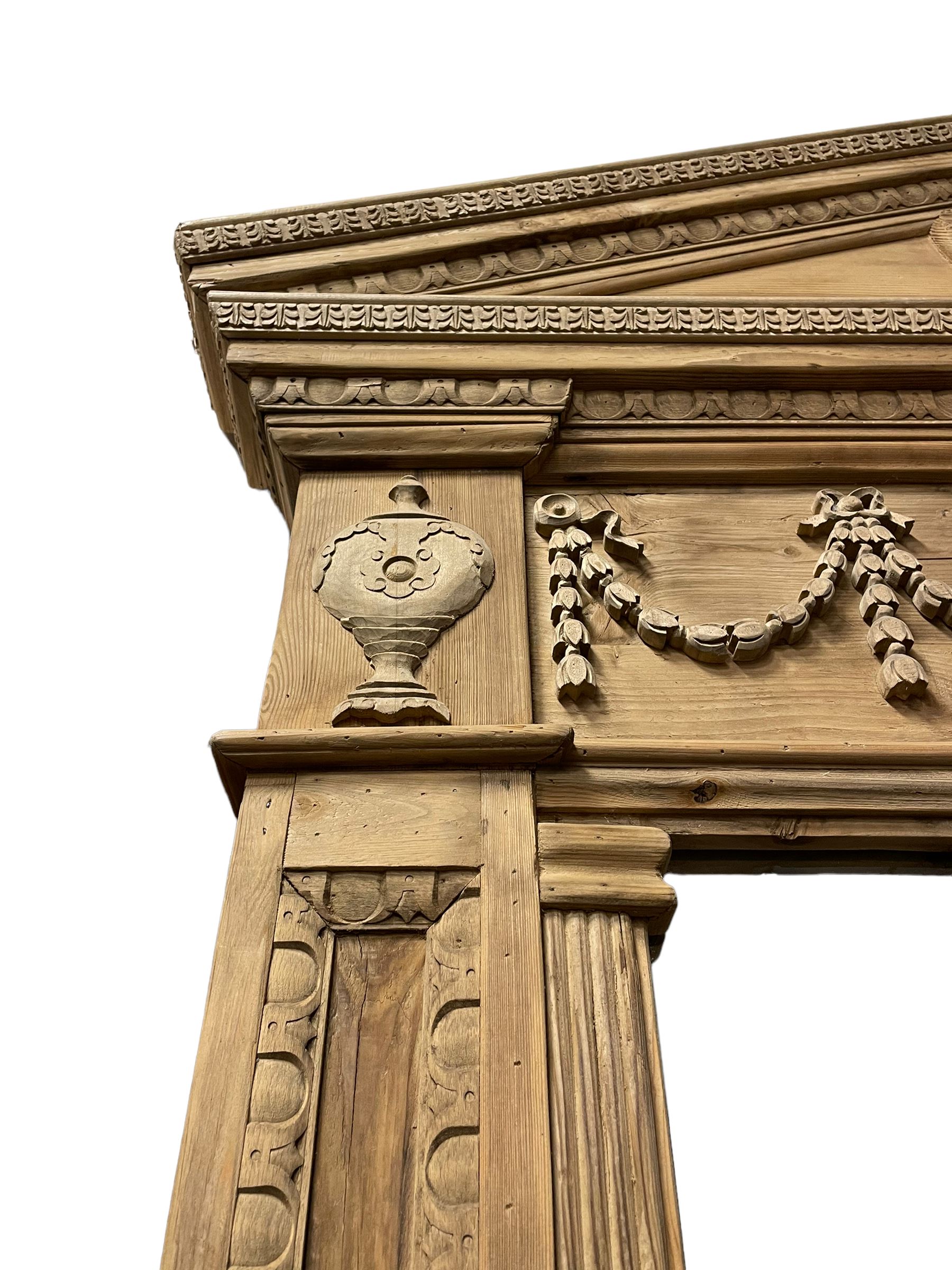 Large Adams design pine frame mirror, sloped broken arch pediment with central acanthus leaf carving, the frieze decorated with bell flower garlands and central kylix vase motif, large plain mirror plate flanked by panelled sides with egg and dart mouldings and reeded slip mouldings, on plinth base