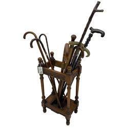 Early 20th century oak stick stand, rectangular structure with decorative carving, square base fitted with tray, on turned supports topped with finials; twelve assorted walking canes 