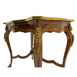 Late 20th century French walnut centre table, the shaped top with inlaid panel depicting musical instrument motifs surrounded by a band of bell flowers, shaped apron mounted with gilt metal scrolling foliage castings, raised on cabriole supports each mounted with foliate cartouche masks, joined by shaped x framed stretchers supporting putto holding floral garland, gilt metal acanthus cast cups and beading 