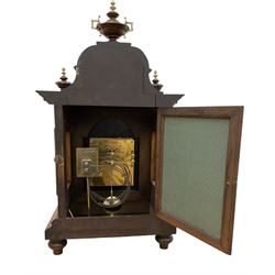 Junghans-German early 20th century walnut cased 8-day mantle clock, with an ogee carved pediment and turned wooden finials, break arch door with brass spandrels beneath flanked by brass caryatids, glazed panels to the sides on a stepped plinth raised on  brass paw feet,  brass dial with a matted centre and silvered chapter with Arabic numerals and Fleur-di Lis steel hands, twin train rack striking movement with a ting tang chime on the quarters. With Key and pendulum. 