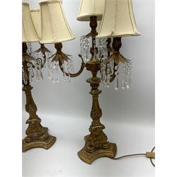 A pair of large gilt table lamps, the foliate and palmette detailed column supporting three curved branches and a central fitting, each supporting clear droppers, and cream shades, upon a trefoil base, H88cm.  