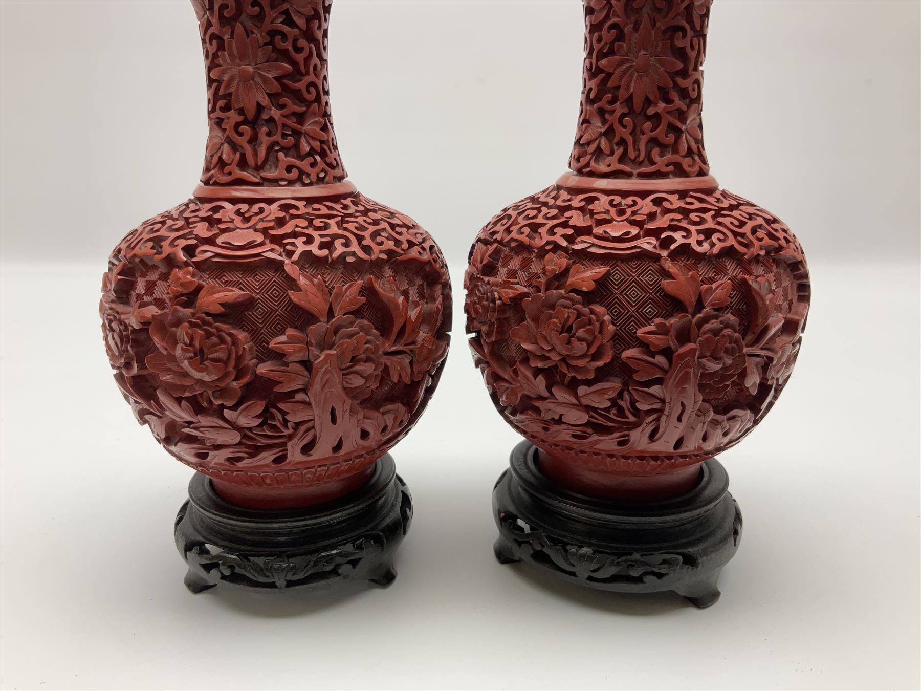 Pair of Chinese cinnabar lacquer vases, each of bulbous baluster form, carved with peonies and foo dogs amongst scrolls, with blue enamel interior and upon wooden bases, H20cm