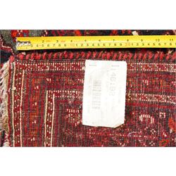 Large Persian Shiraz crimson ground carpet, the busy field decorated with a geometric pole medallion surrounded by stylised plant motifs with contrasting indigo spandrels and geometric-woven guard bands