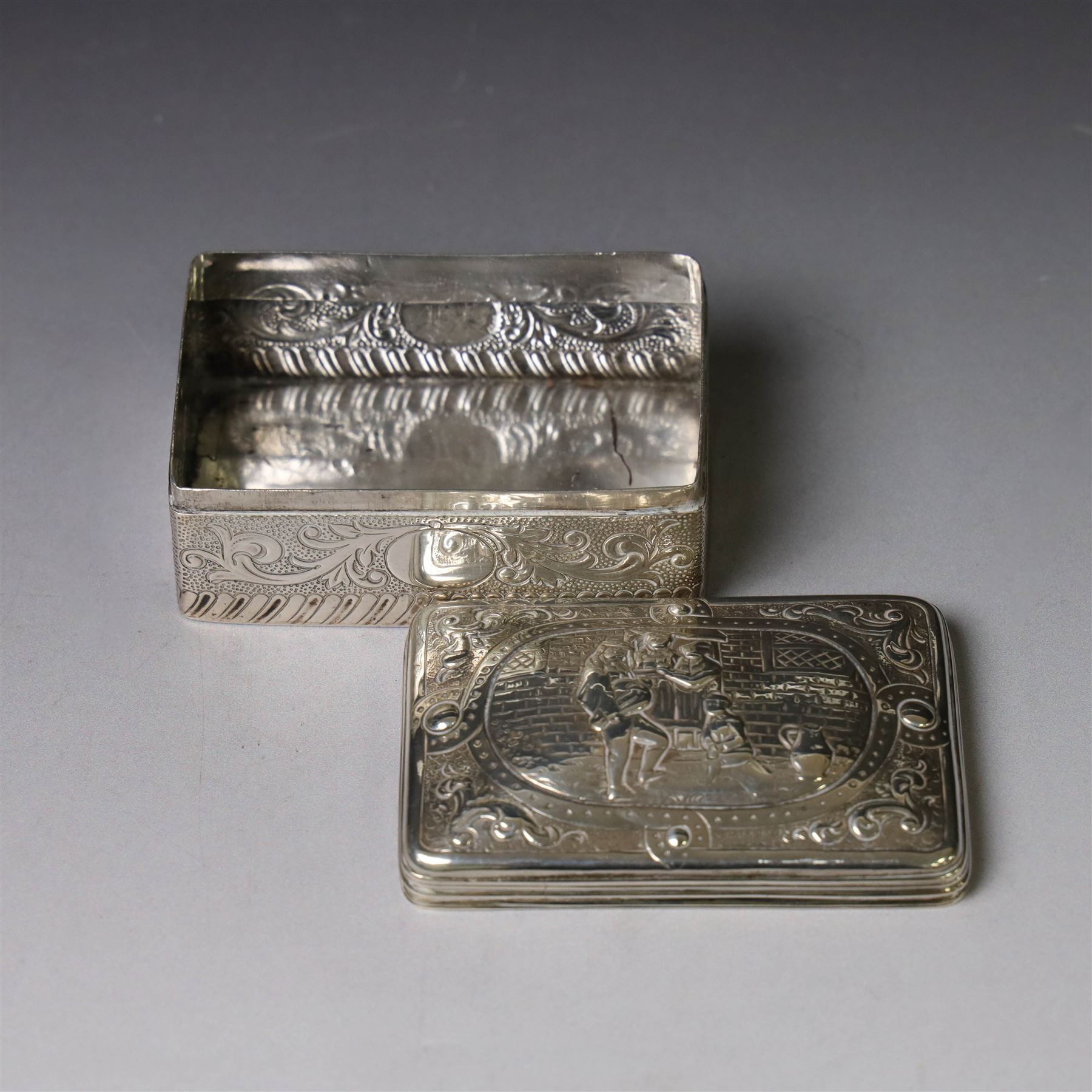 19th century Continental silver box, of rectangular form, the lift off cover with repousse figural scene, the base chased with vacant panels, acanthus scrolls and flower heads, unmarked, H4.5cm W8.5cm D5.5cm