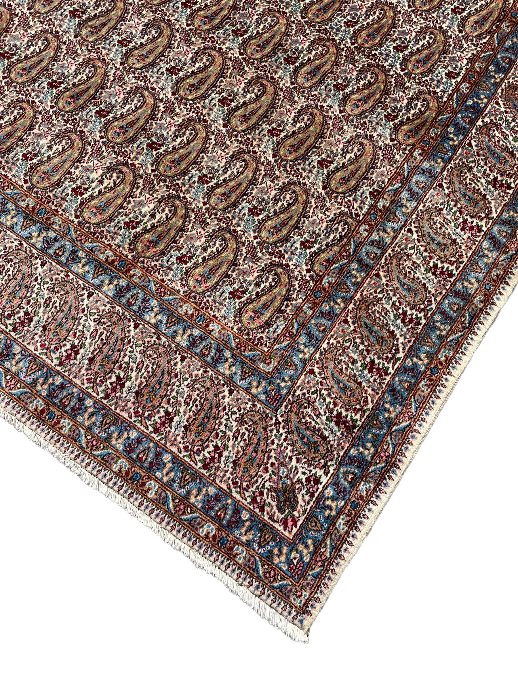 Persian Kirman carpet, the ivory ground field and border decorated with repeating Boteh motifs, interspaced with all-over floral design, blue ground border guards, the top border with signature panel