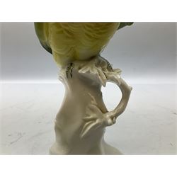 Karl Ens porcelain figure of a parrot, modelled with yellow breast, blue back and wings and green tail, perched upon on a blossoming branch, with blue printed factory mark beneath, H24.5cm