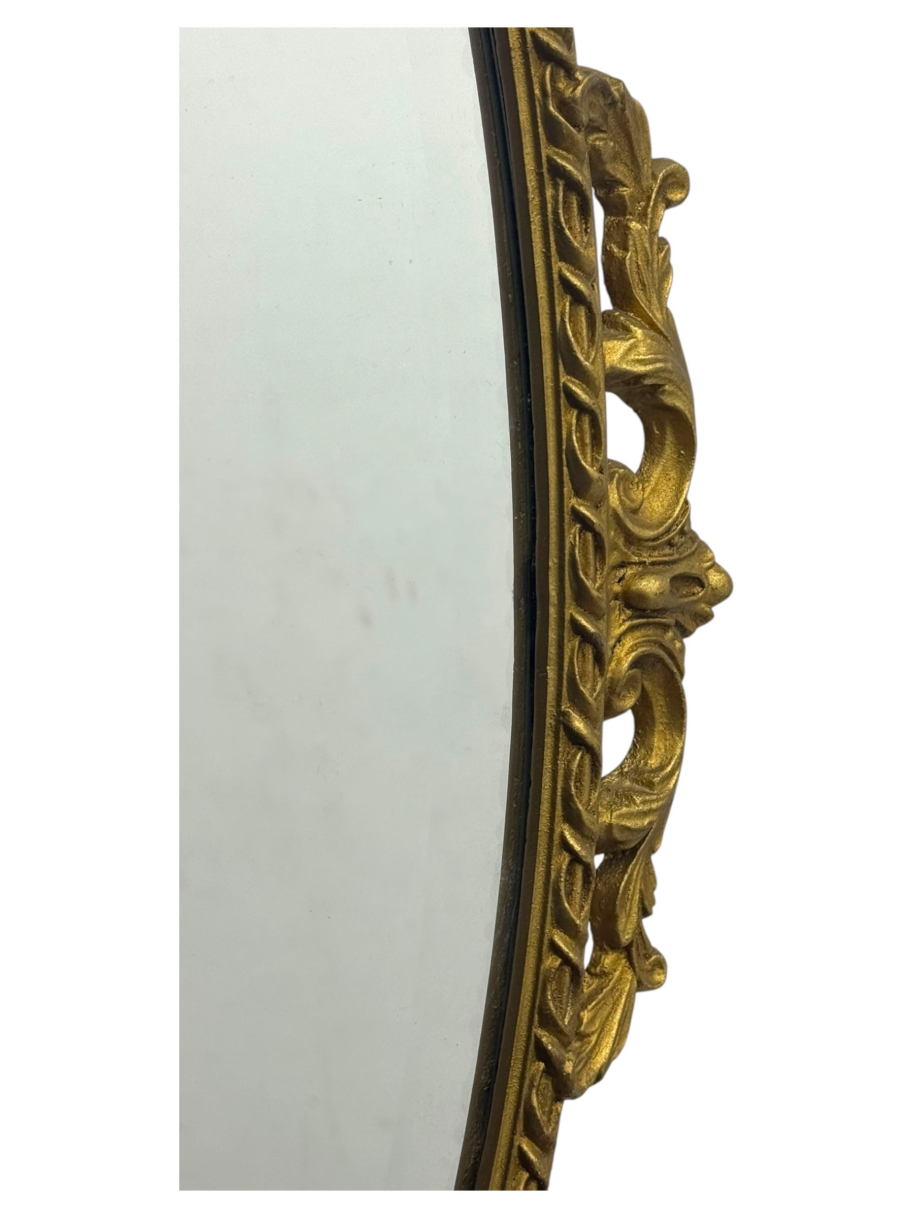 Oval gilt wall mirror, with bevelled edge plate within a moulded frame cast with acanthus scrolls and foliate decoration, pierced cartouche crest and apron, flanked by scrollwork handles