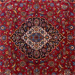 Central Persian Kashan hand-knotted carpet, rich crimson red field with a central cusped medallion with finely drawn floral sprays surrounded by dense scrolling vine work and palmettes, framed by a broad indigo ground border of flowering arabesques flanked by multiple guard stripes, in a palette of red, blue, ivory, sage green, and soft ochre tones, with cotton fringe ends    