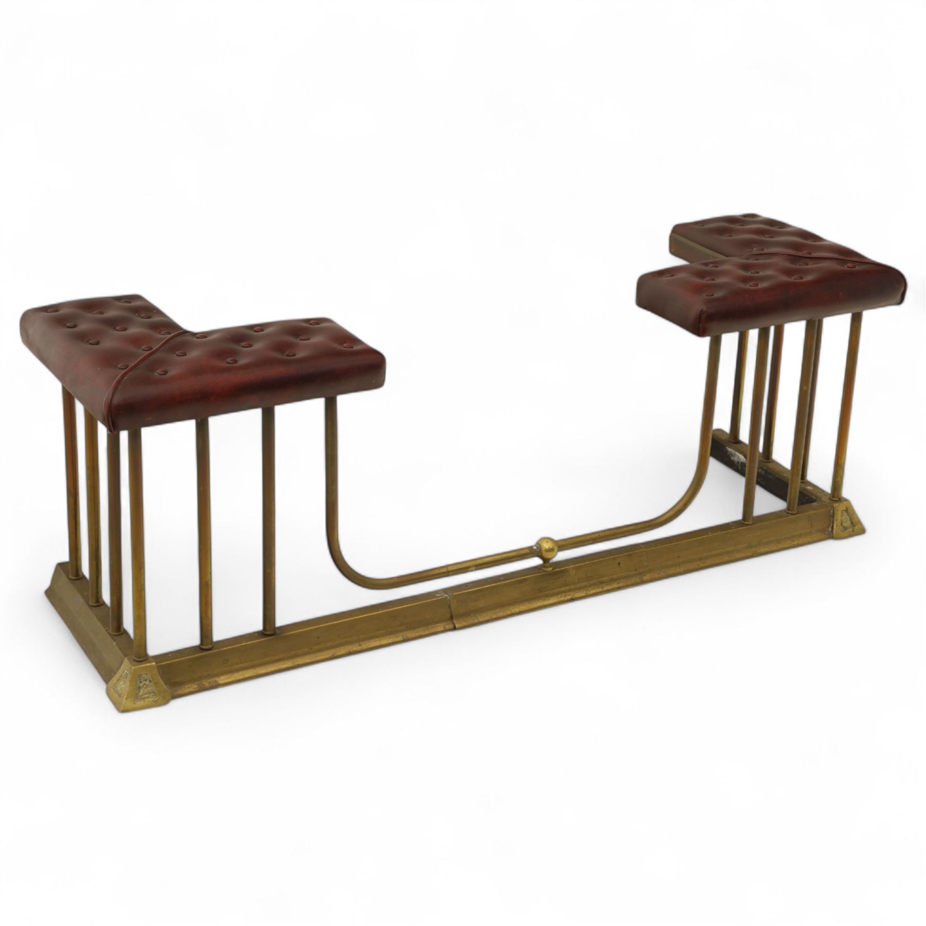 Late Victorian brass and cast iron club fender, burgundy leather buttoned seat pads, secured by bar uprights at the front and back, and a cross stretcher held in place by further bar uprights on a chamfered platform base, circa 1890, internal base dimensions 127cm 