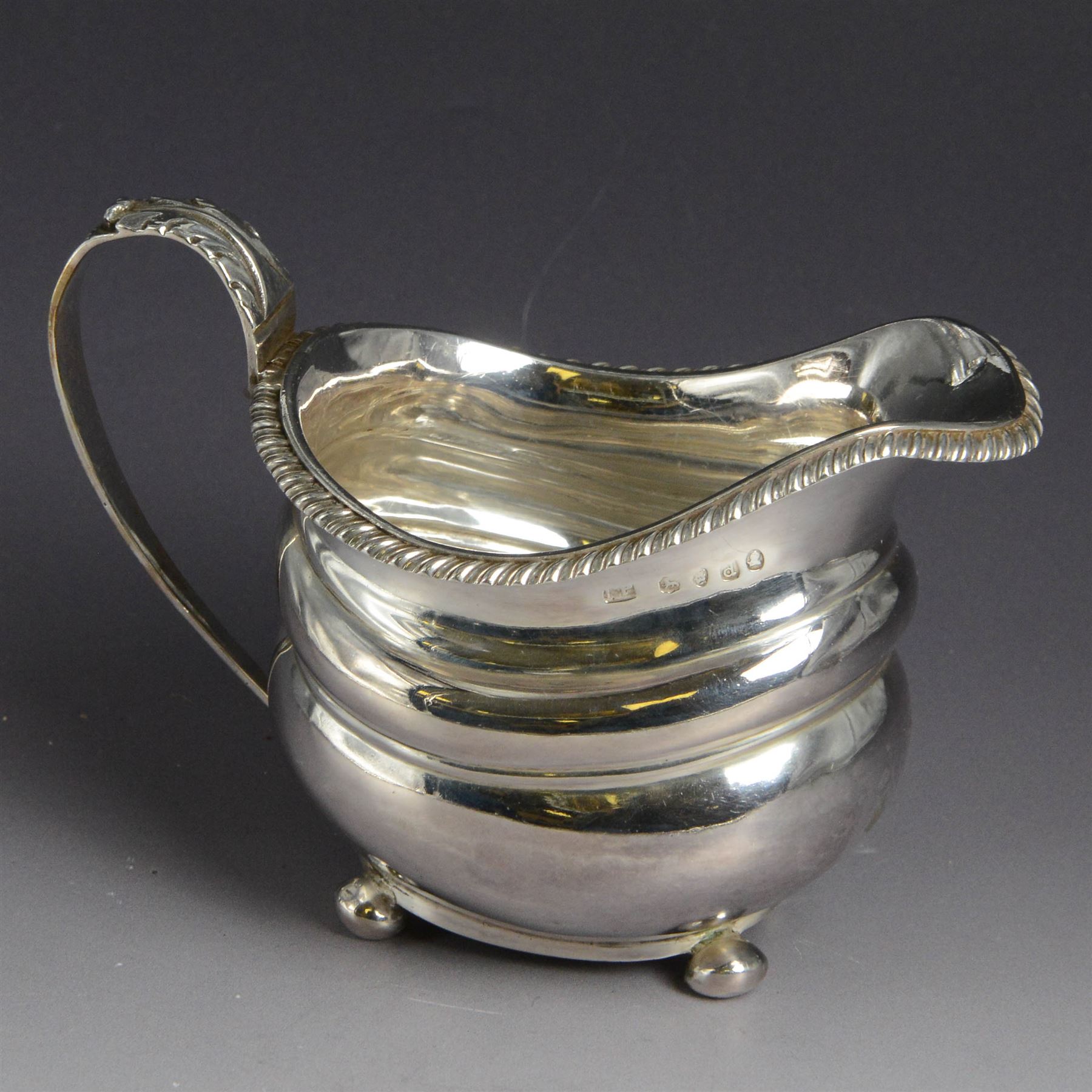 George III silver milk jug, of oval form with oblique gadrooned rim and acanthus leaf capped handle, upon four bun feet, hallmarked London 1819, maker's mark worn and indistinct, H10cm