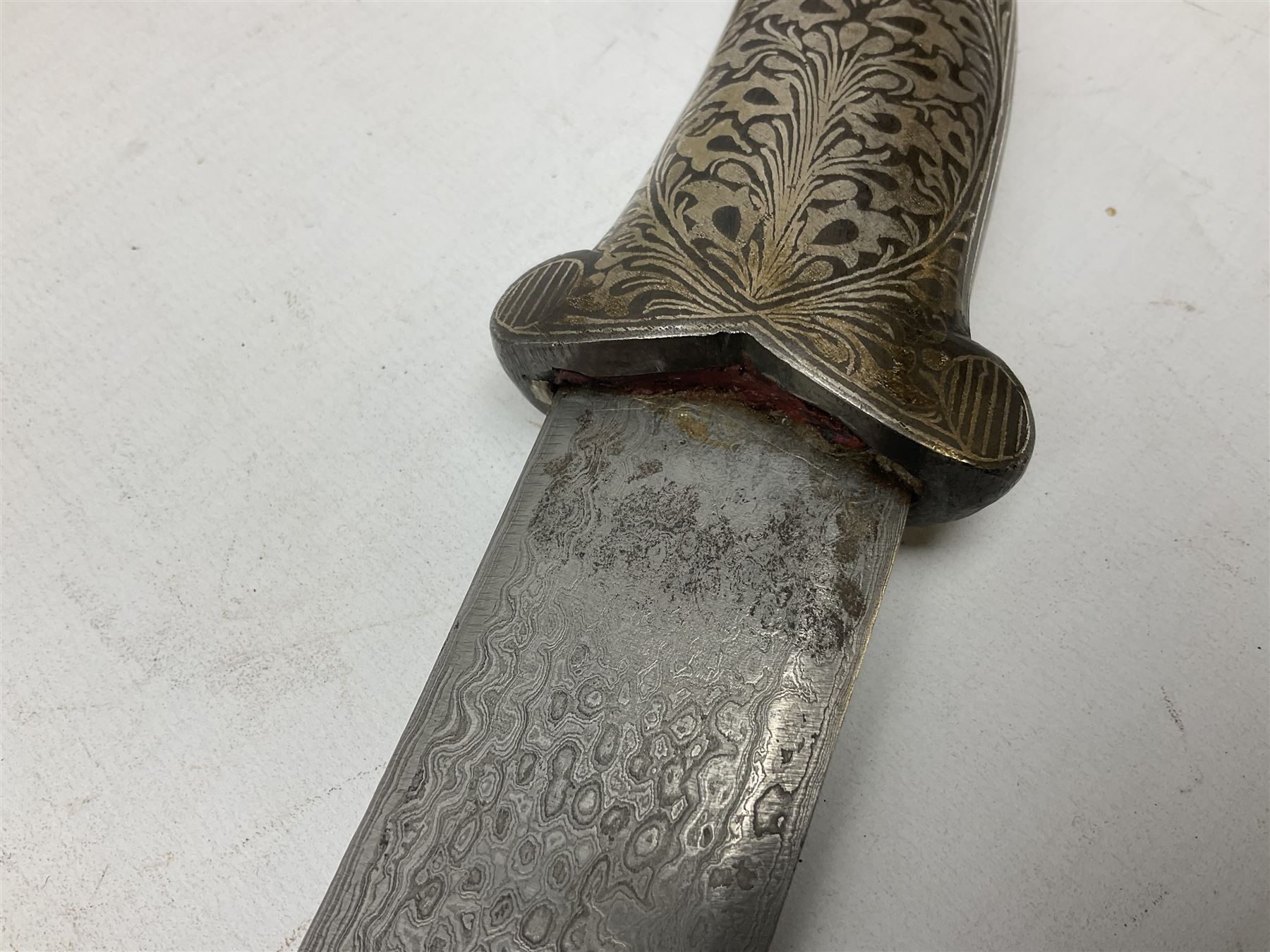 Indian Khanjar dagger with 28cm curving damascus steel blade inlaid with silver floral emblem, white metal and niello style grip in the form of a bird's head with pronounced beak and matching scabbard L44cm overall