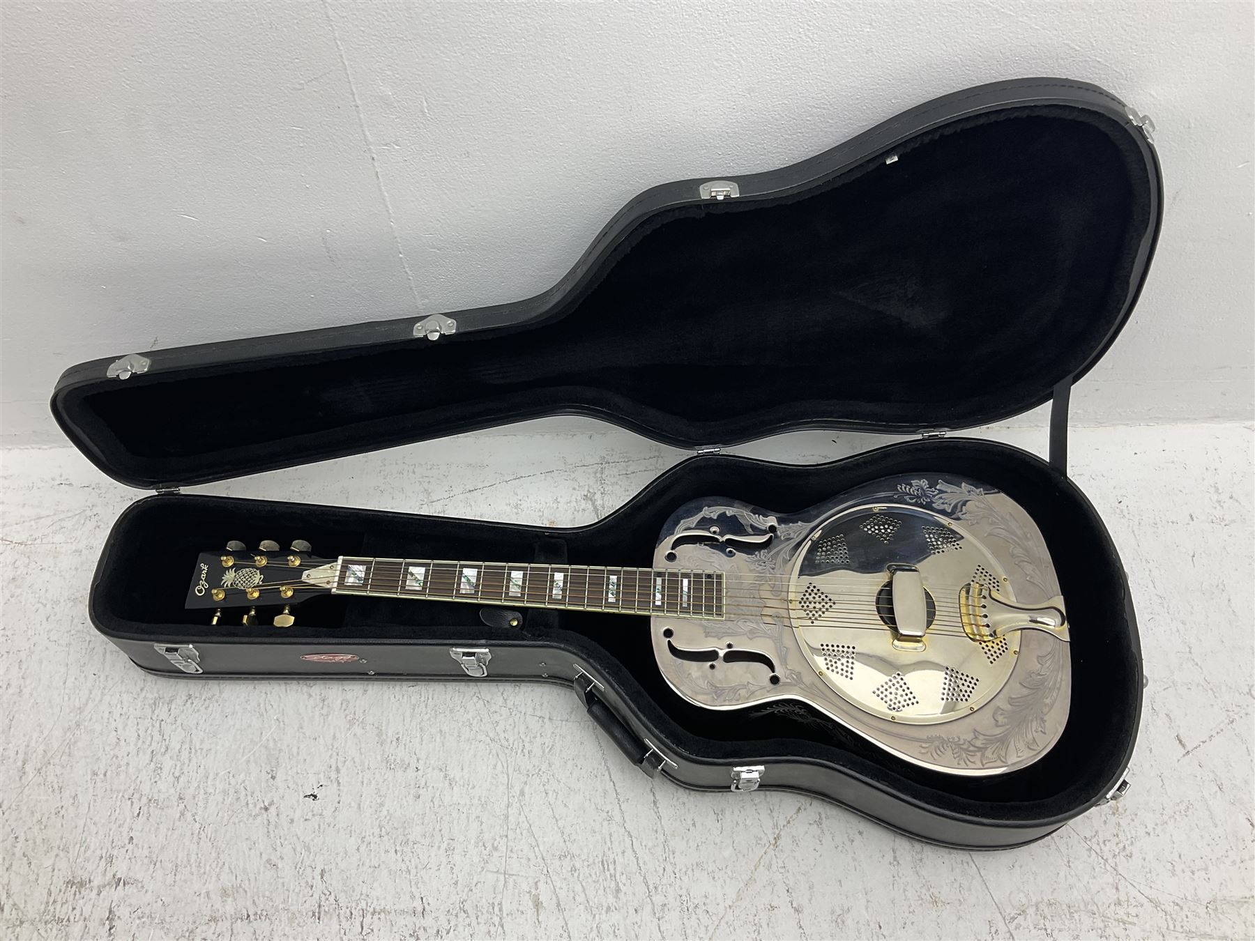 Ozark metal cased resonator guitar with all over chased foliate decoration to the polished finish and mother-of-pearl inlay to the fretboard L100cm; in Stagg hard carrying case