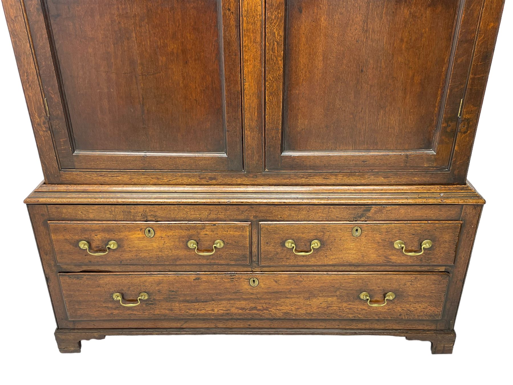 George III oak livery cupboard, projecting moulded cornice over two panelled doors, the upper panels within stepped ogee and arched moulded frame, the interior fitted with a single row of wooden hooks, two short and one long drawers, on bracket and return skirted base 