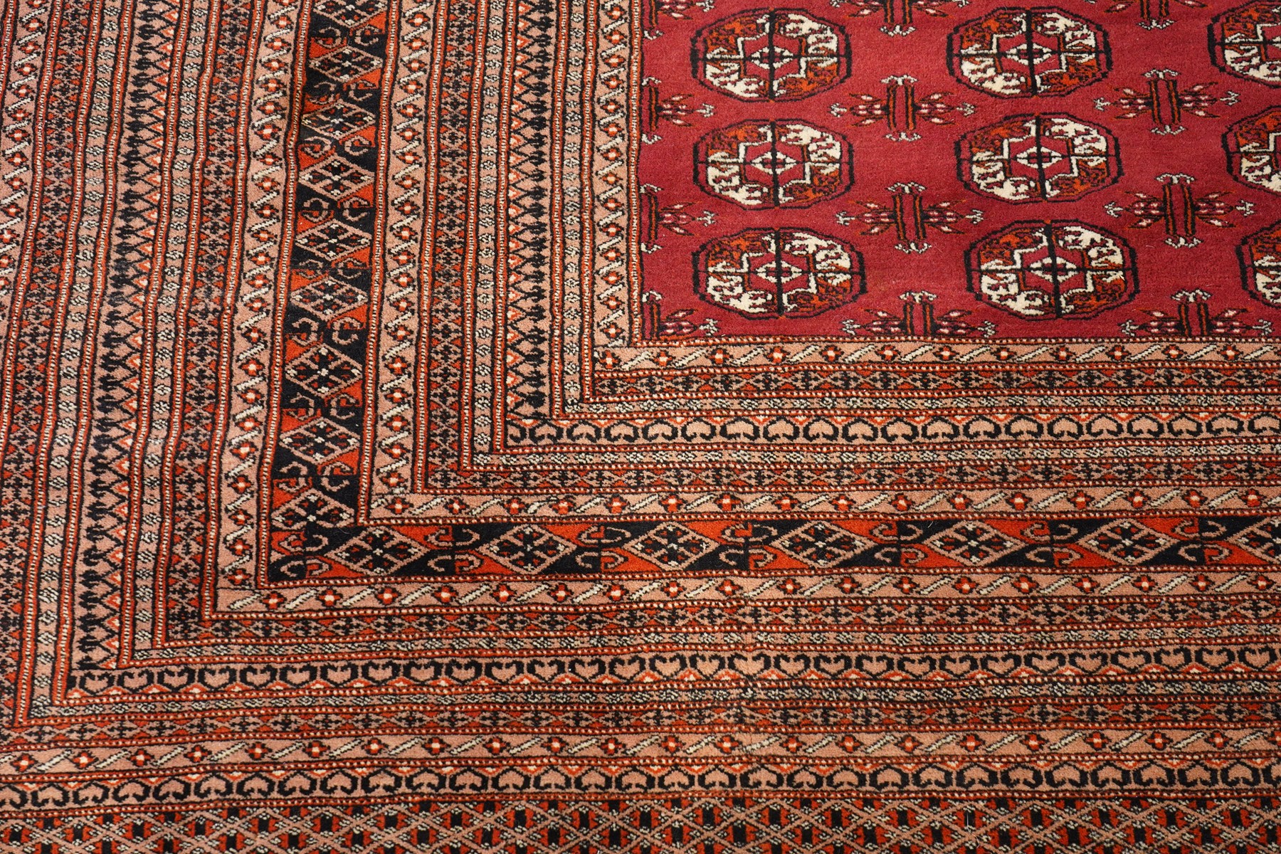 Large Afghan Bokhara crimson ground carpet, the field with rows of repeating Gul motifs and geometric design, enclosed by multiple repeating geometric guard bands