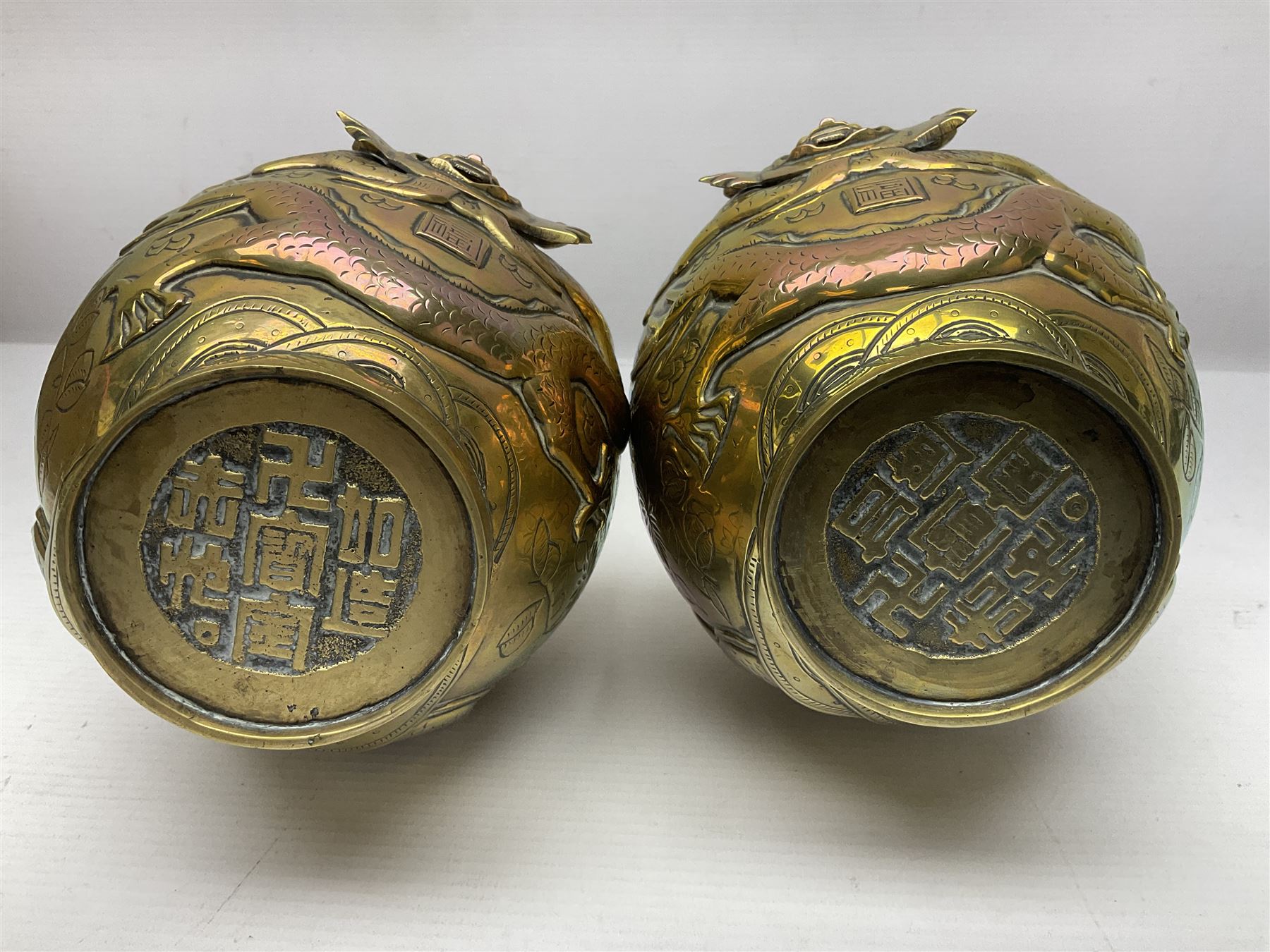 Pair of Chinese brass vases, of ovoid form with elongated neck and fluted rim, decorated in high relief with a dragon chasing a flaming pearl around the neck, the body with dragons, birds and buildings, with character marks beneath, H25cm