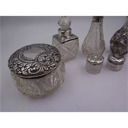 Two silver mounted dressing table jars, one in the form of a heart, both with embossed silver covers and cut glass bodies, hallmarked, together with two smaller examples, one set with mother of pearl, three silver mounted glass scent bottles, including an example with prunus blossom decoration, stamped Sterling, tallest bottle H17cm