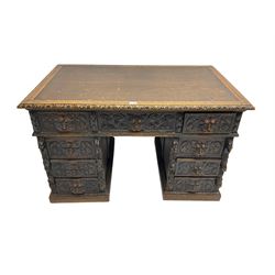 Late 19th century Gothic revival carved oak twin pedestal desk, rectangular top with inset writing surface and carved edges, central frieze drawer flanked by eight drawers, all with green man carved handles and extending trailing foliage, carvings of pineapple and lion mask corbels, the pedestals with panelled sides and back, on plinth bases