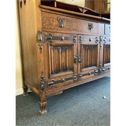 Shapland and Petter - Arts & Crafts period oak dresser, raised gallery top with spade balustrade, central bevelled mirror flanked by two cabinet, astragal glazed doors with yellow tinted glass and bullseye panes, the sides with pierced heart shaped decoration, fitted with two drawers and two double cupboards, enclosed by linenfold panelled doors,  copper work strap hinges and fixtures, on shaped spade feet, the locks stamped 'S&P'