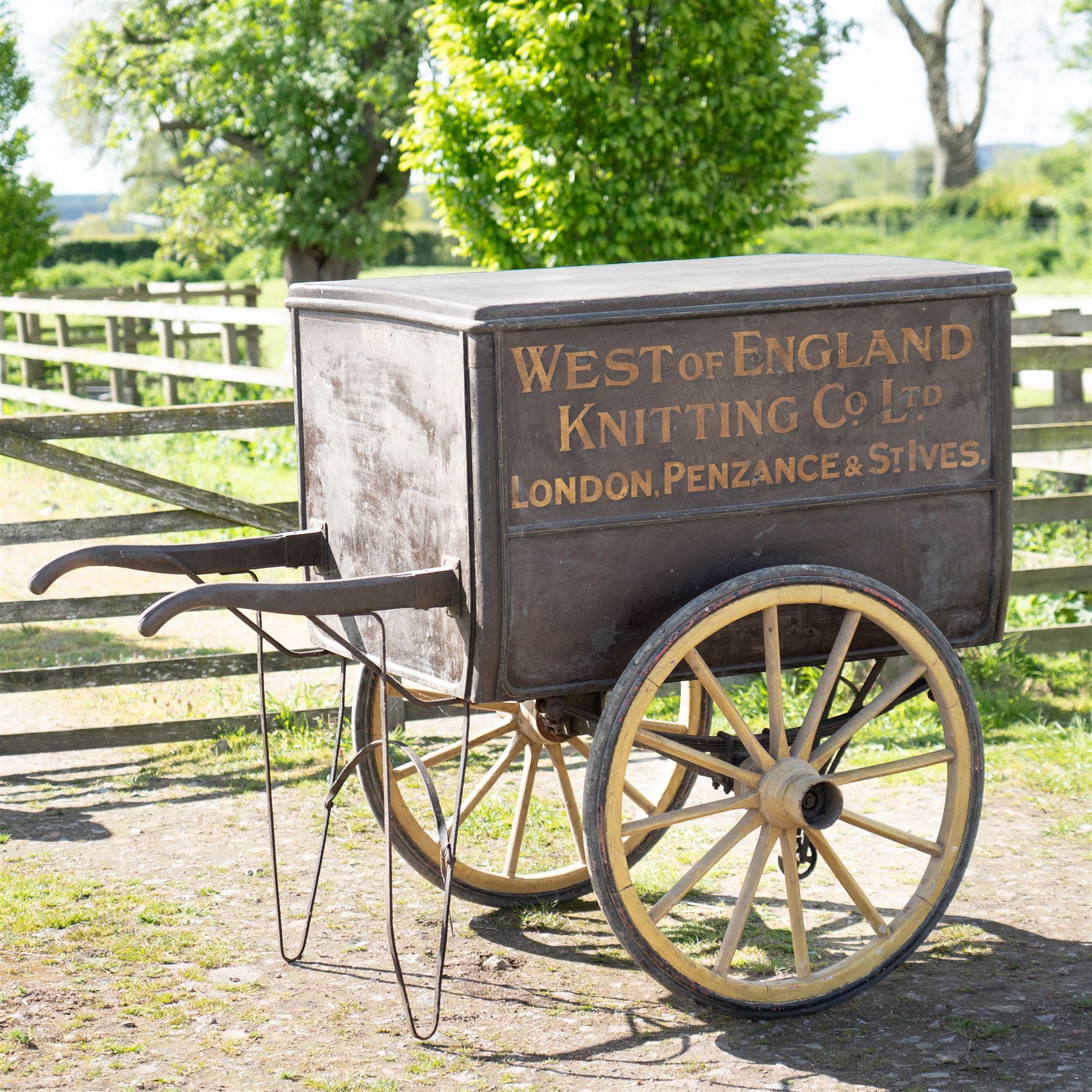 West of England Knitting Co. Ltd. Advertising Hand Cart

A rare and highly decorative late Victorian or Edwardian advertising hand cart, retaining its original black painted finish and gilt signwriting for West of England Knitting Co. Ltd., London, Penzance & St Ives. The enclosed box body is mounted on large cream painted wooden spoked wheels and fitted with rear push handles, allowing the cart to be manoeuvred by hand. Intended as a promotional and delivery vehicle for one of Britain's best known knitwear manufacturers, the cart survives as an evocative piece of commercial advertising history. The interior remains accessible via twin rear doors, while traces of the original maker's transfer for the Warwick Carrier are visible. An unusual and attractive display piece suited to collectors of advertising, transport memorabilia and social history.

Features

• Original hand painted gilt signwriting for West of England Knitting Co. Ltd.
• Advertising panels referencing London, Penzance and St Ives
• Enclosed wooden box body with twin rear access doors
• Original black painted finish with period lettering
• Large cream painted wooden spoked wheels with iron tyres
• Rear push handles for hand propelled operation
• Warwick Carrier maker's transfer remains visible
• Original undercarriage and running gear
• Attractive display piece with strong commercial advertising appeal
• Suitable for museum, retail, interior or collection display

Dimensions:
Overall length: 190 cm
Body length: 125 cm
Overall width: 140 cm
Body width: 100 cm
Height: 150 cm

Wheel Diameter:
Wheels: 92 cm