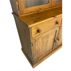 Large pine bookcase on cupboard, the upper section enclosed by two glazed door, the lower section fitted with two drawers and double cupboard, on plinth base