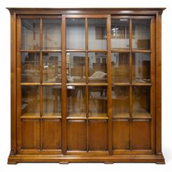 Wesley Barrel - large cherry wood bookcase, with projecting cornice and fielded panelled sides, with three sections comprising three fixed shelves, sliding glazed and panelled doors, moulded plinth base