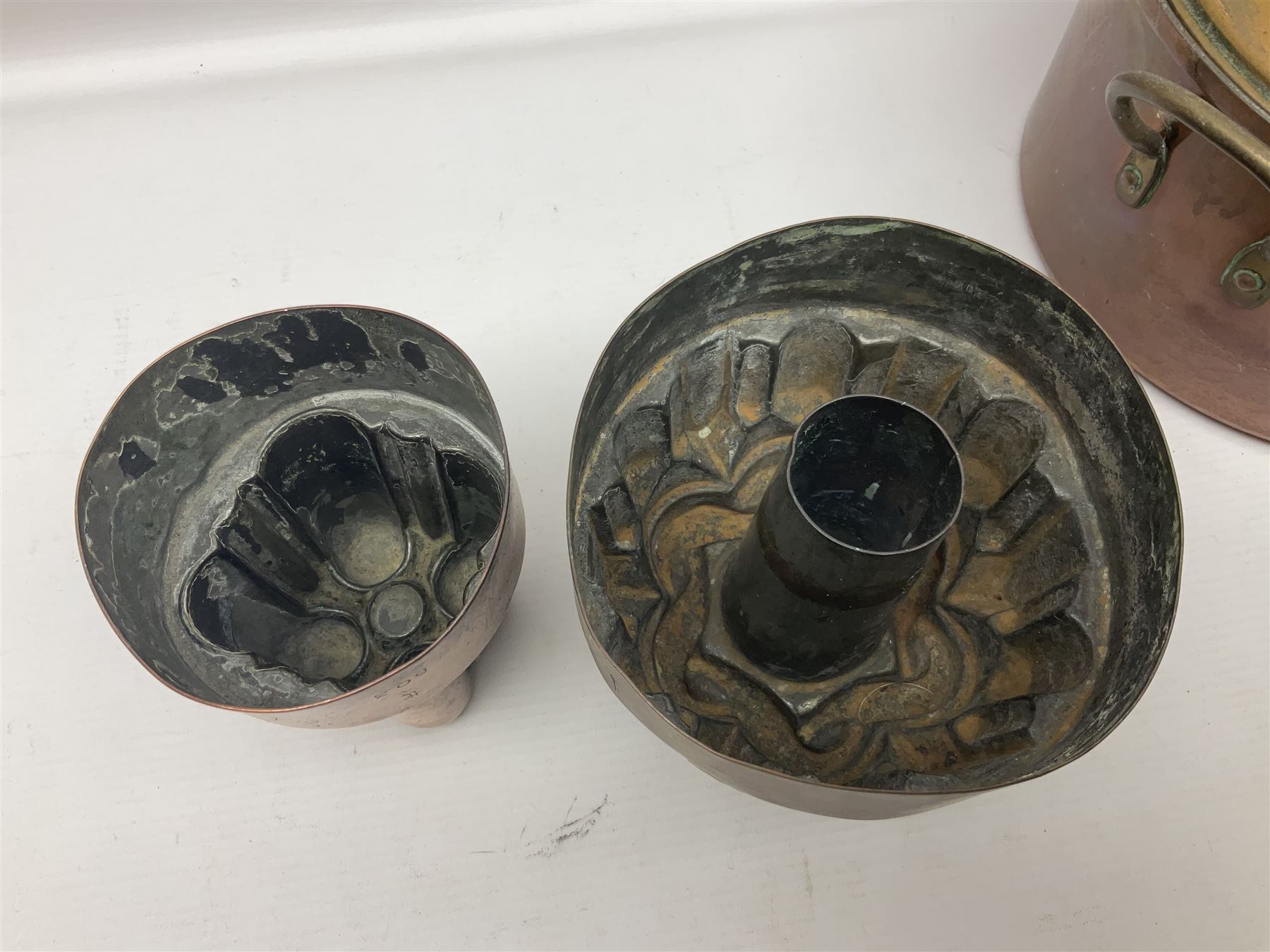 Four Victorian copper moulds, together with a graduating set of copper pans with wooden handles and finials to covers, largest pan 