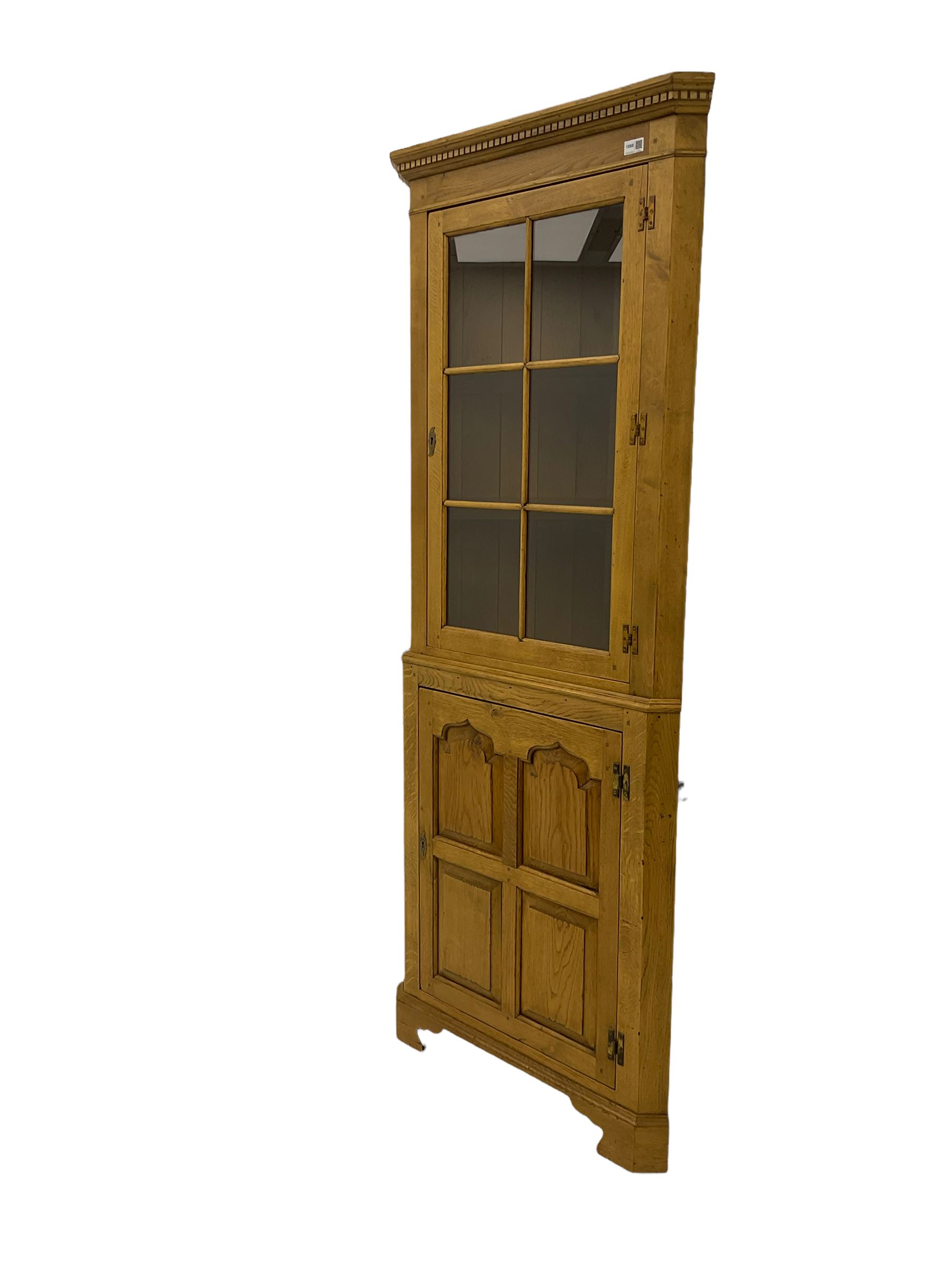 Traditional light oak corner cabinet, projecting cornice, dentil frieze, single glazed door above single fielded door