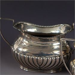 Victorian silver bachelors teapot, of part fluted oval form with ebonised wooden handle and finial, hallmarked Thomas Bradbury & Sons, London 1896, together with a Edwardian silver milk jug and open sucrier, of similar form with oblique gadrooned rims, hallmarked George Unite, Birmingham 1902 & 1906