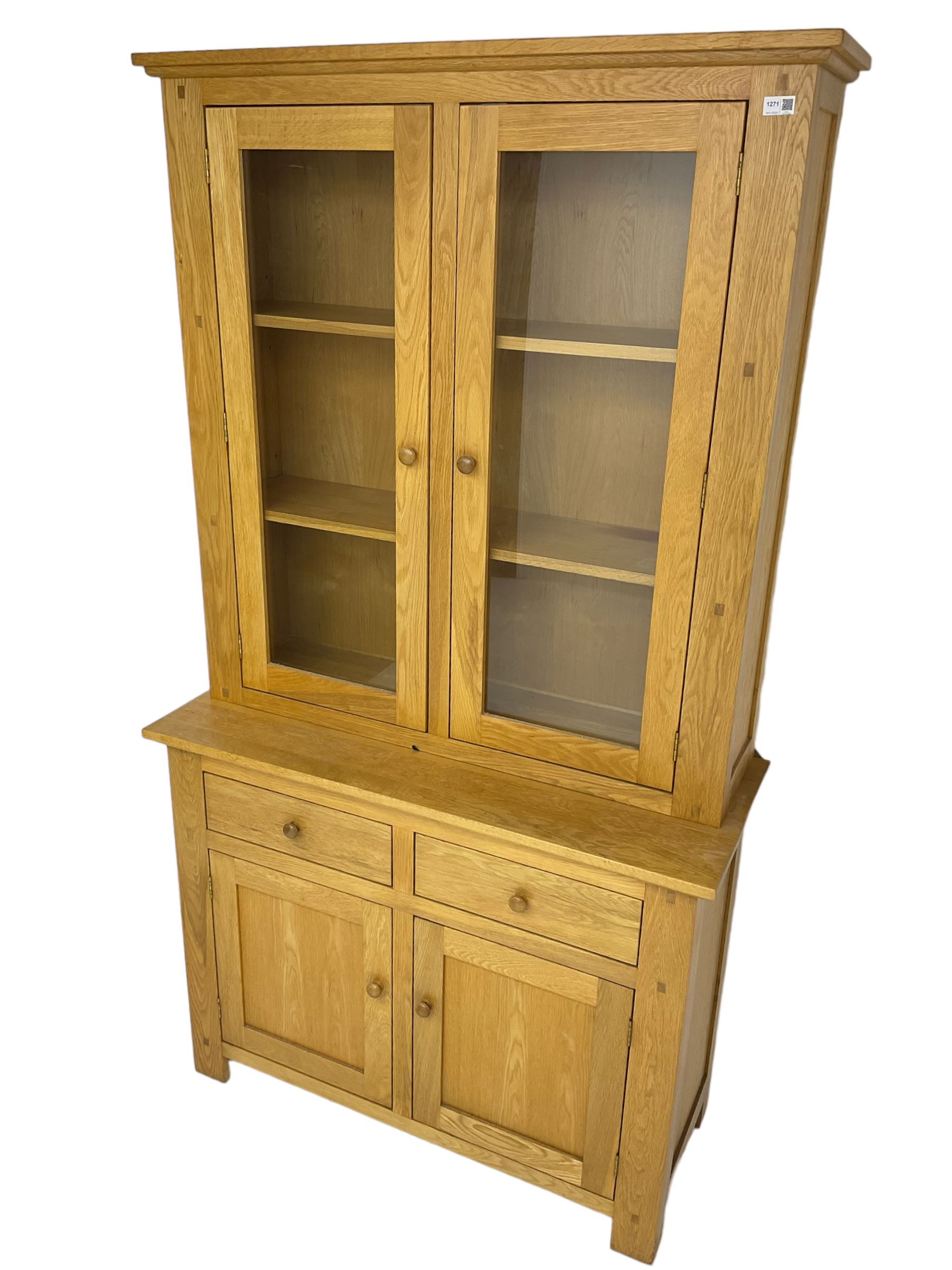 Contemporary light oak bookcase display cabinet, fitted with  two glazed doors enclosing two shelves, above two drawers and cupboards