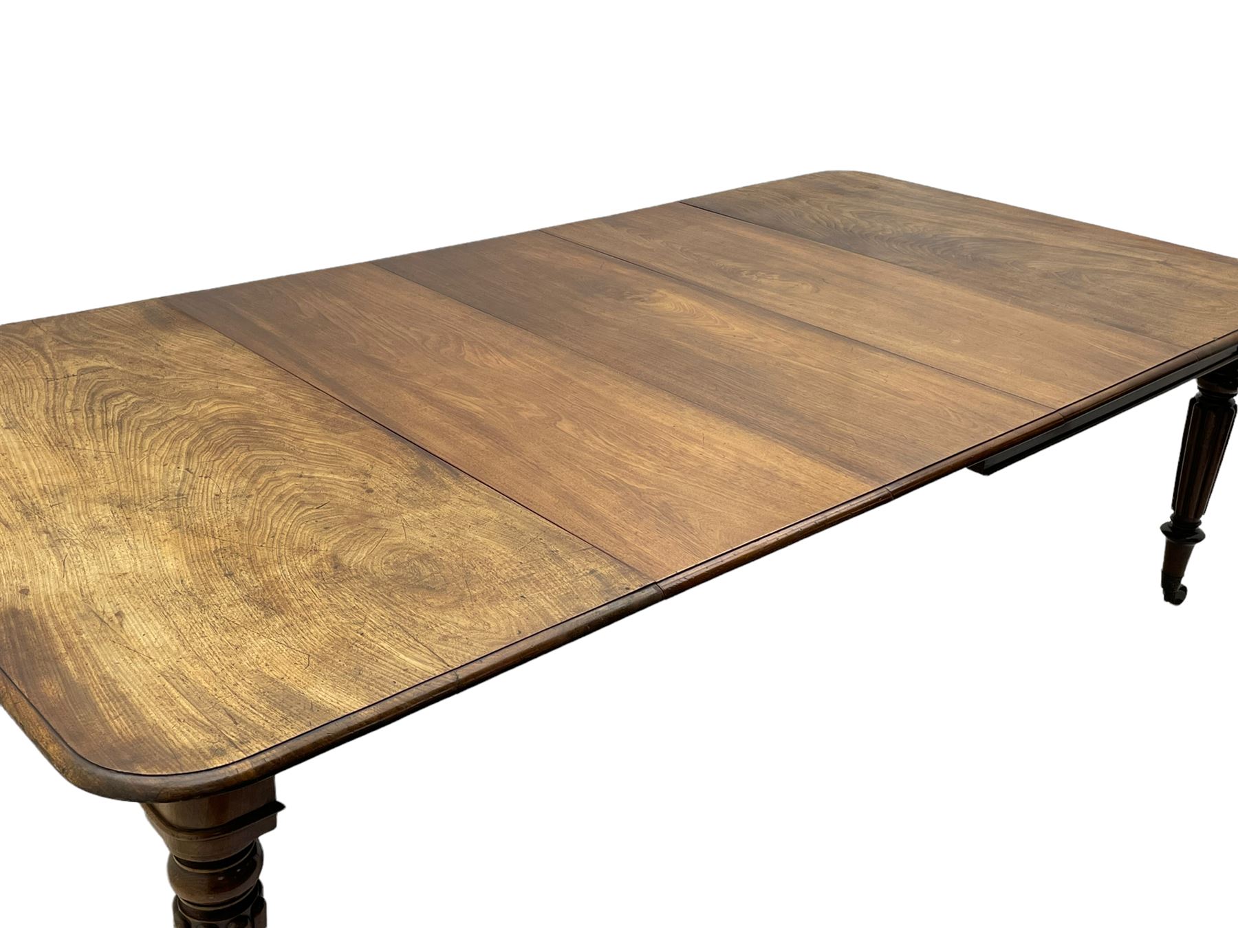 Early 19th century figured mahogany extending dining table, the rectangular top with moulded edge and rounded corners, pull-out action with three additional leaves, raised on turned and lobe carved supports with brass cup castors