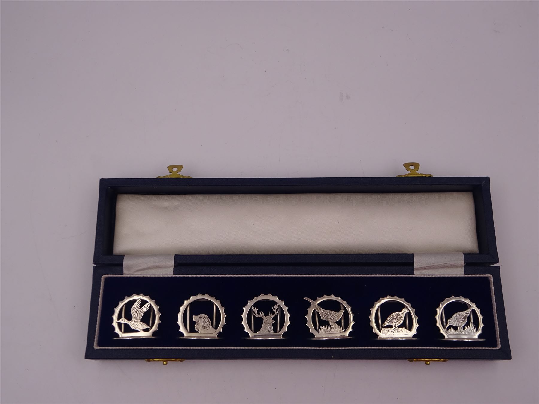 Set of six modern silver place card holders, each of circular form with pierced depictions of a partridge, spaniel, pheasant, stag, woodcock and duck, hallmarked J A Campbell, London 1985, contained within a velvet and silk lined fitted case, H3cm