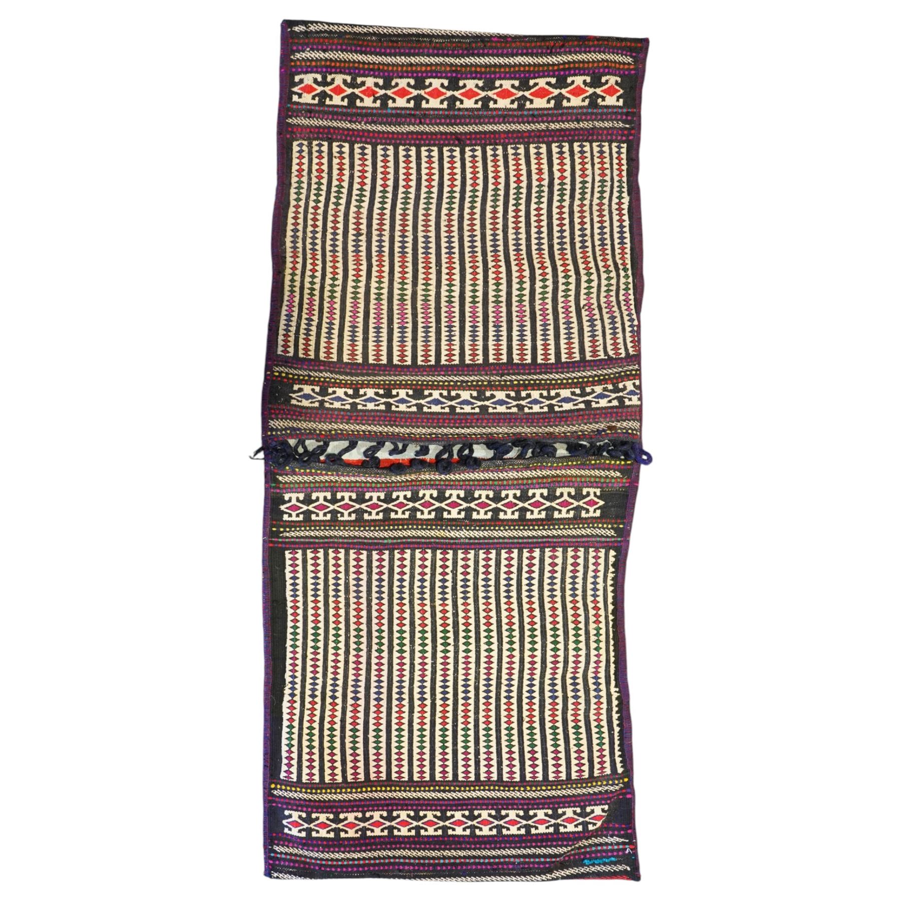 North East Persian Turkoman saddle bag, traditional double pouch form, each panel woven with vertical bands of small geometric motifs on ivory ground, framed by multiple horizontal borders of angular tribal ornament of hooked devices and steeped lozenges, reverse with stripped coloured flatweave bands 