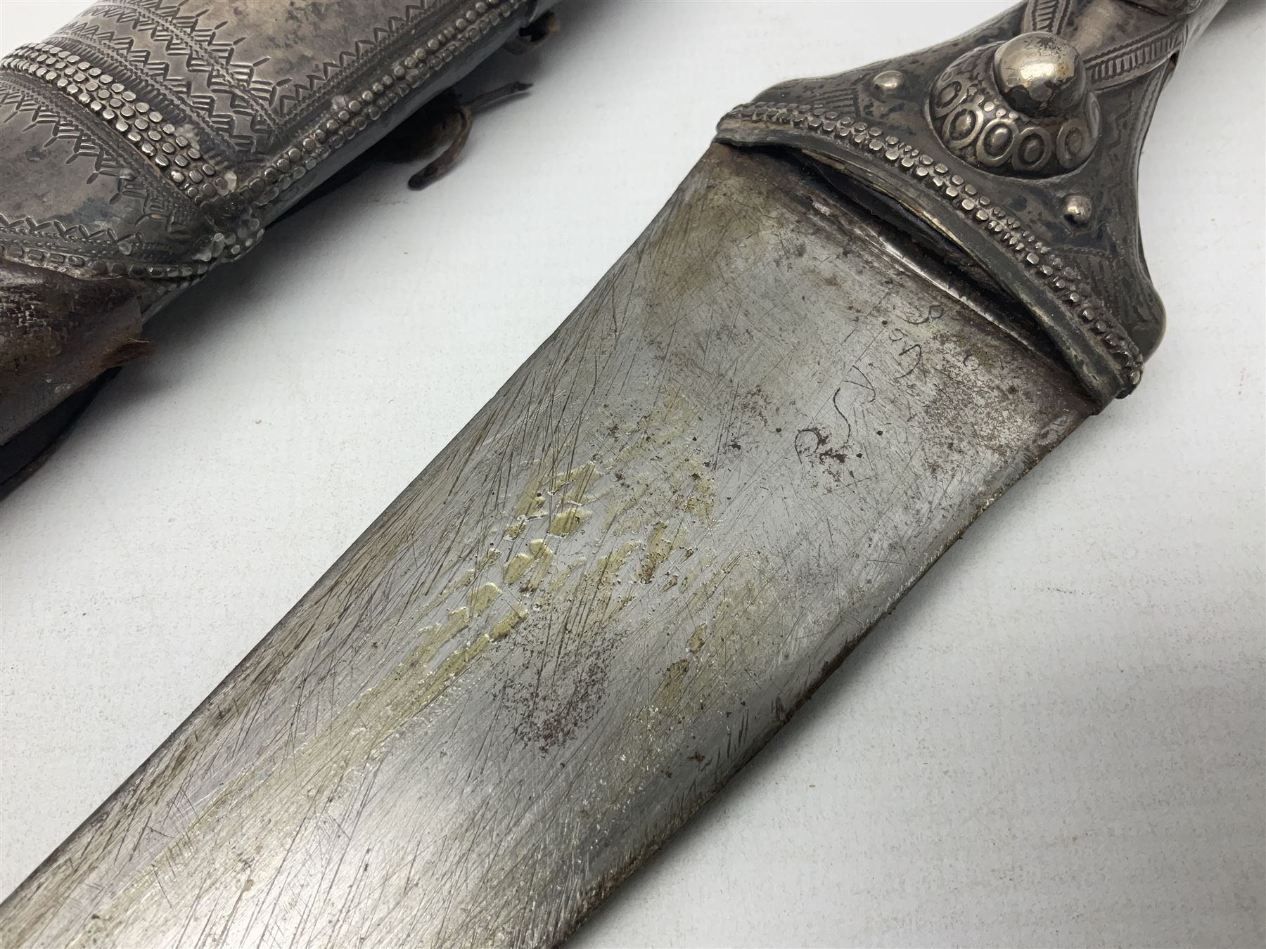 Late 19th/20th century Middle Eastern jambiya dagger the 36cm broad curved double edged steel blade with traces of script, horn and copper backed waisted white metal hilt with three roundel buttons; in ornate white metal and leather mounted brass and steel scabbard L60.5cm overall