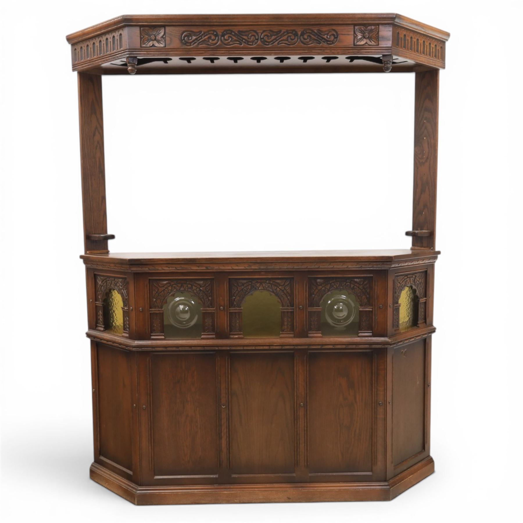 Old Charm - carved oak bar with three bar stools and associated Old Charm drinks cabinet, carved top with channels for glassware beneath, bar surface above glazed panels, shelves for glassware to the back, associated Old Charm drinks cabinet with fall front linenfold carving, above twin doors with shelved interior