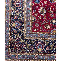 Northeastern Persian Meshed hand-knotted carpet, madder red field with an all-over design of scrolling vines, palmettes, and rosettes, within a dark blue border of palmettes and arabesques 